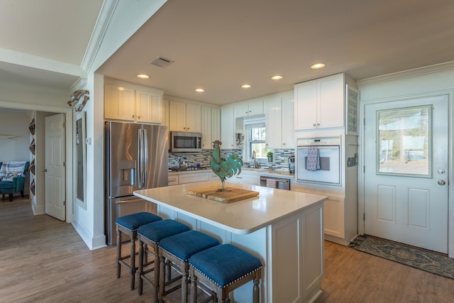 kitchen with white cabinetry, a kitchen bar, a center island, stainless steel appliances, and light hardwood / wood-style flooring