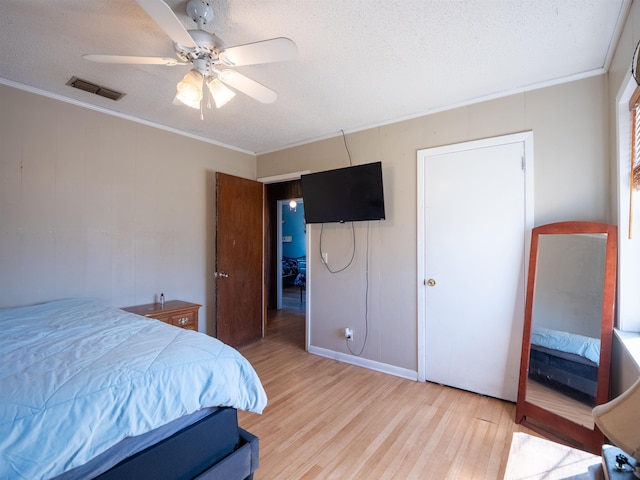 bedroom featuring a textured ceiling, ornamental molding, light wood-type flooring, and visible vents