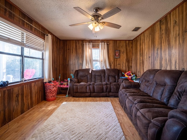 living area featuring wood walls, ceiling fan, visible vents, and light wood finished floors