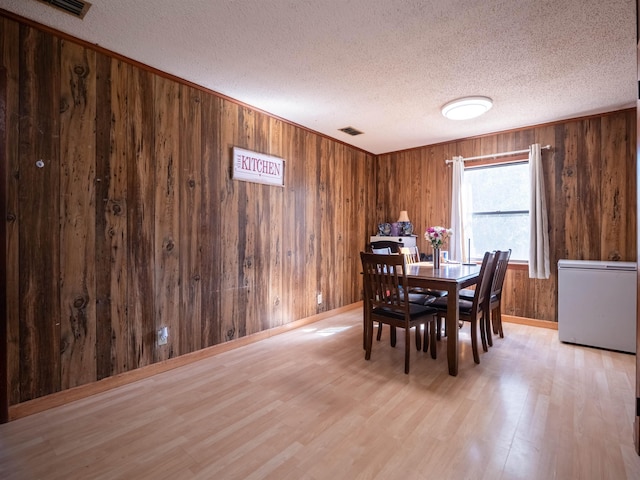 dining room featuring wooden walls, visible vents, a textured ceiling, and light wood finished floors