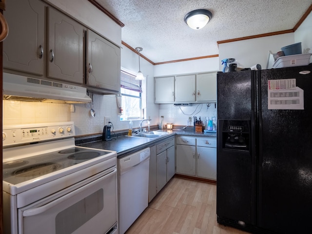 kitchen featuring white appliances, dark countertops, crown molding, under cabinet range hood, and a sink