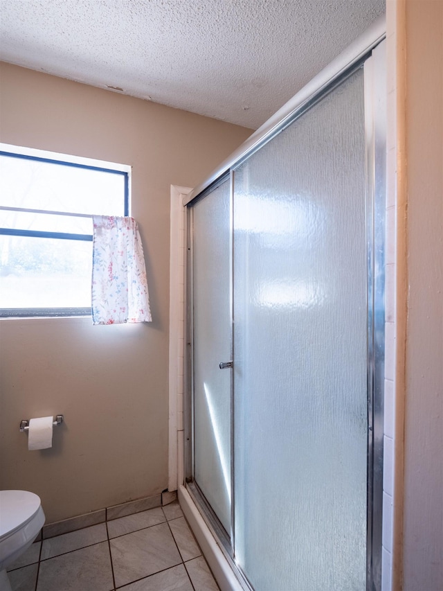 bathroom with toilet, a shower stall, a textured ceiling, and tile patterned floors