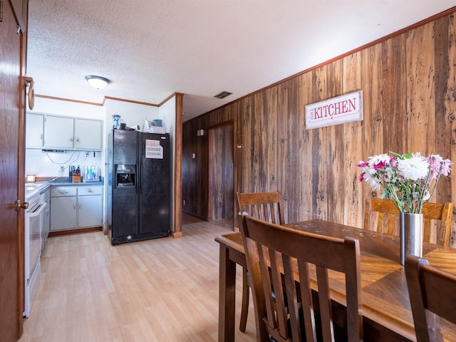 dining space with wooden walls, visible vents, light wood-style flooring, a textured ceiling, and crown molding