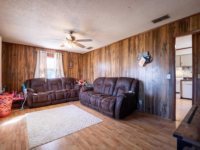 living area featuring a textured ceiling, light wood-style flooring, wood walls, visible vents, and a ceiling fan