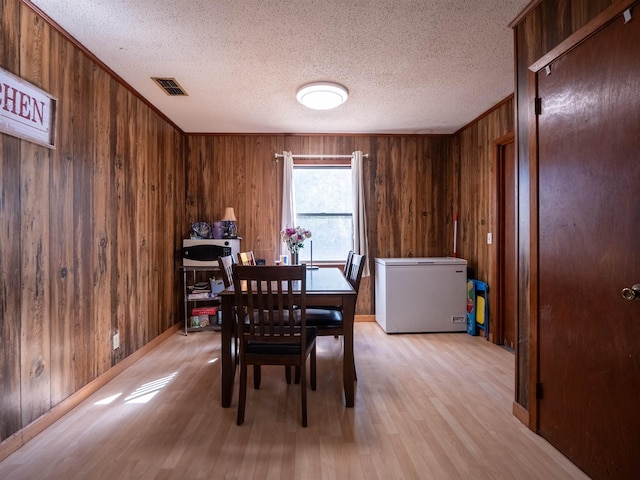 dining room with visible vents, ornamental molding, a textured ceiling, wood walls, and light wood-style floors