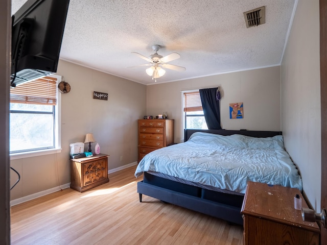 bedroom with a textured ceiling, ceiling fan, visible vents, light wood-style floors, and ornamental molding