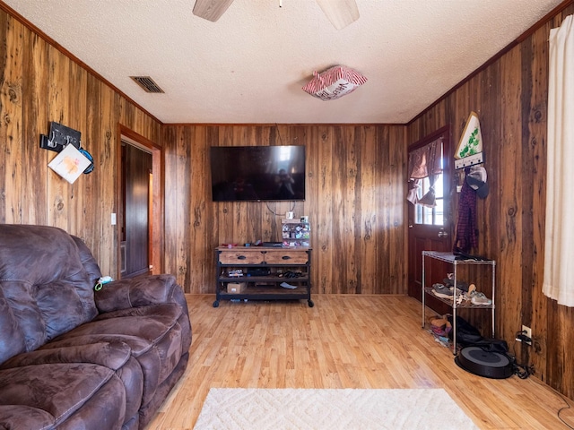 living area with ornamental molding, visible vents, a textured ceiling, and light wood finished floors