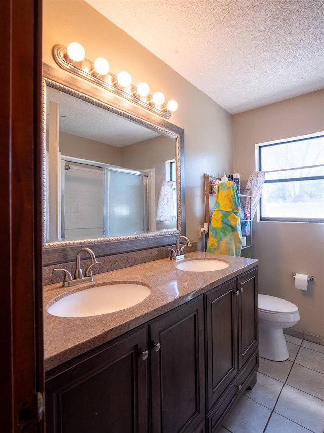 bathroom with a textured ceiling, double vanity, a stall shower, and a sink