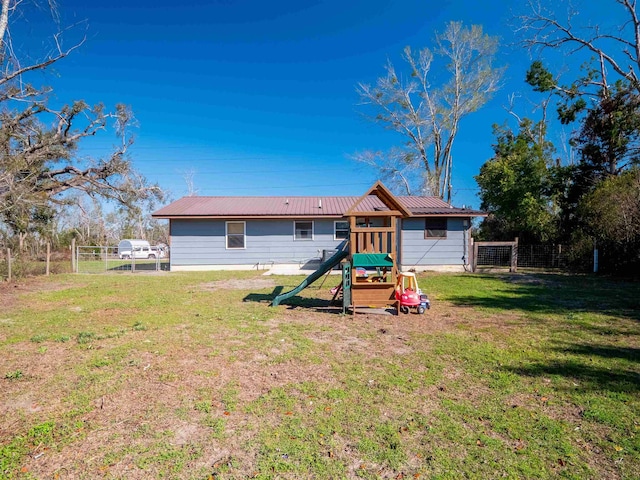 rear view of house with fence, metal roof, a playground, and a yard