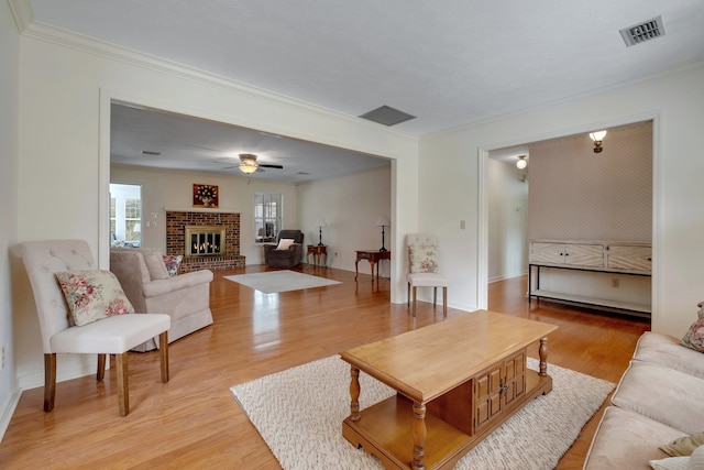 living room featuring ceiling fan, light wood-type flooring, crown molding, and a brick fireplace