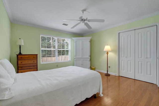 bedroom with ceiling fan, light wood-type flooring, crown molding, and a closet