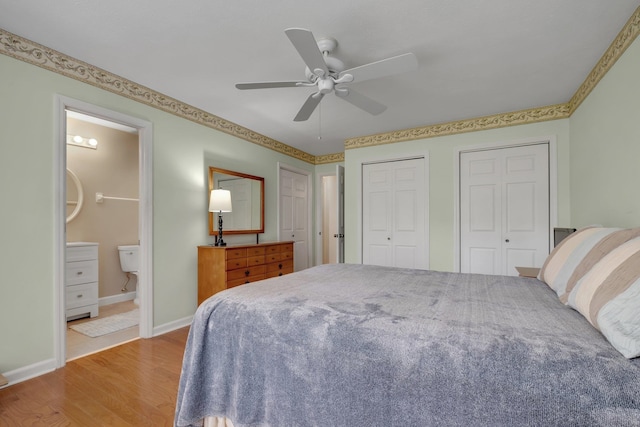 bedroom featuring light wood-type flooring, ensuite bathroom, ceiling fan, and multiple closets