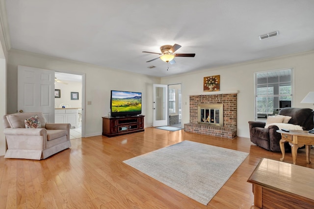 living room with a brick fireplace, crown molding, ceiling fan, and light wood-type flooring