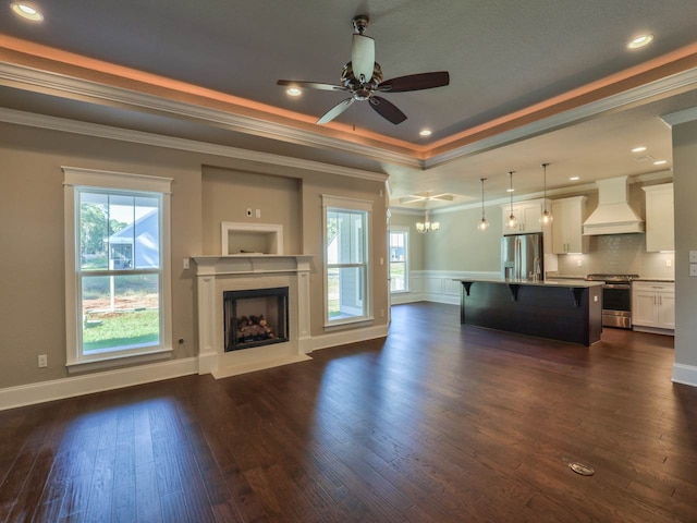 unfurnished living room featuring a raised ceiling, dark wood-type flooring, ceiling fan, and crown molding