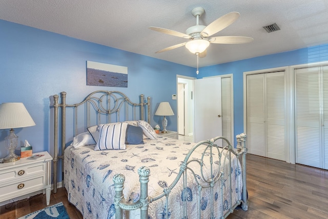 bedroom featuring a textured ceiling, dark hardwood / wood-style flooring, ceiling fan, and multiple closets