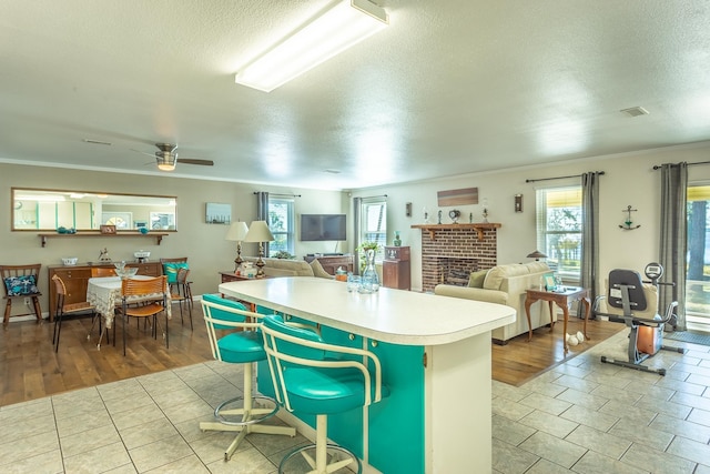 kitchen featuring a brick fireplace, ceiling fan, a textured ceiling, and light hardwood / wood-style flooring