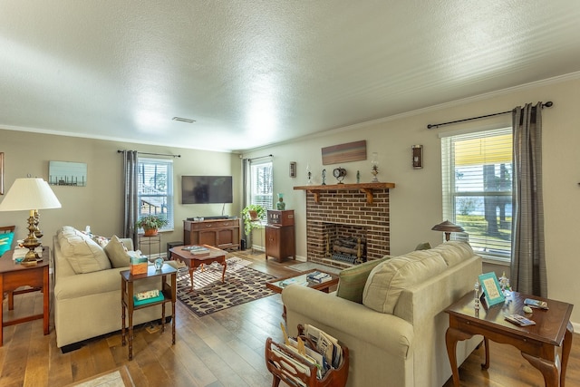 living room featuring hardwood / wood-style floors, a textured ceiling, a brick fireplace, and ornamental molding