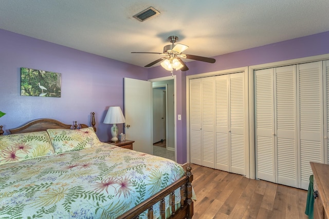 bedroom with a textured ceiling, ceiling fan, two closets, and hardwood / wood-style flooring