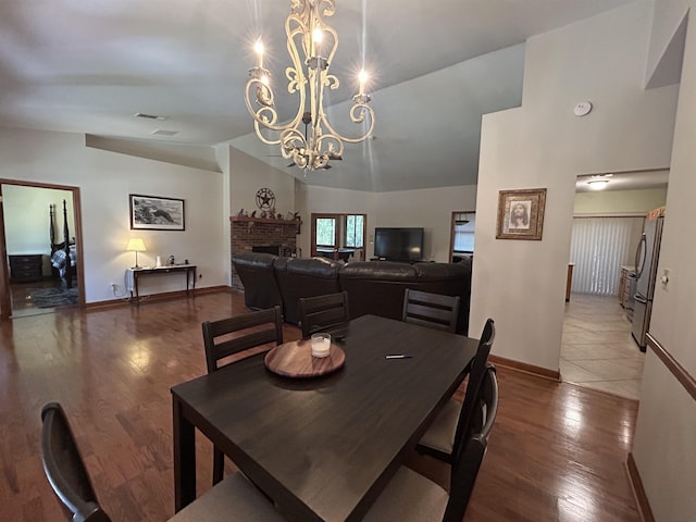 dining room with a fireplace, a notable chandelier, vaulted ceiling, and wood-type flooring