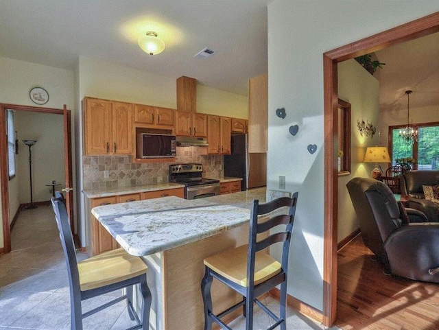 kitchen with appliances with stainless steel finishes, decorative light fixtures, a breakfast bar area, decorative backsplash, and kitchen peninsula