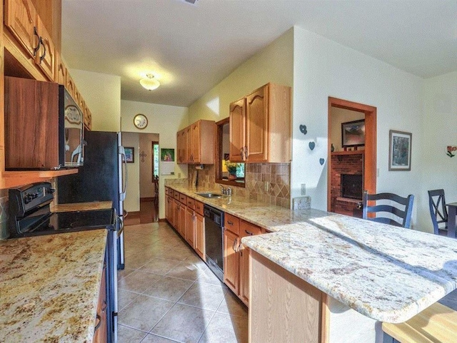 kitchen with a breakfast bar, black appliances, a brick fireplace, kitchen peninsula, and backsplash