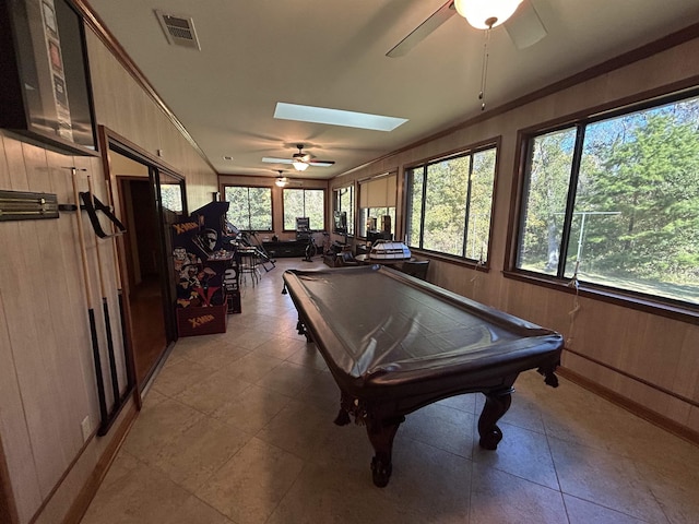 game room with crown molding, a skylight, wooden walls, and a healthy amount of sunlight