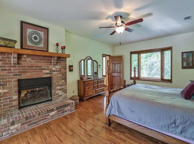 bedroom featuring wood-type flooring, a brick fireplace, and ceiling fan