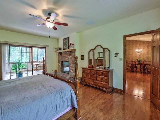 bedroom with access to exterior, ceiling fan with notable chandelier, a fireplace, and dark wood-type flooring