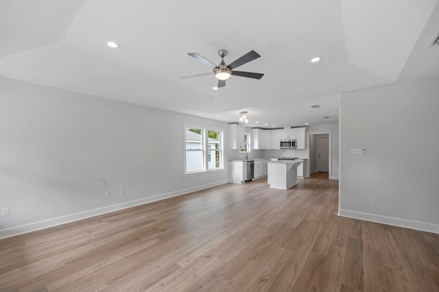 unfurnished living room featuring a tray ceiling, ceiling fan, and light wood-type flooring