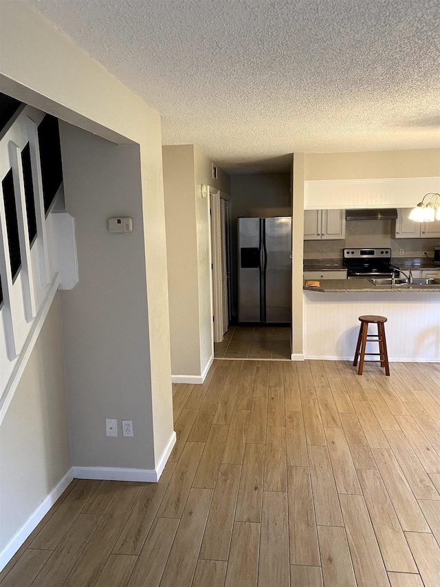 2247 Shady Timbers Cir Unit C, Tallahassee, FL 32304 - kitchen with stainless steel appliances, wood finished floors, a textured ceiling, wall chimney exhaust hood, and a kitchen breakfast bar