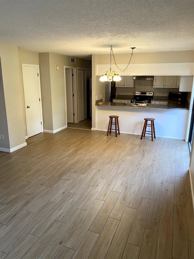 2247 Shady Timbers Cir Unit C, Tallahassee, FL 32304 - kitchen featuring stainless steel range with electric stovetop, wood finished floors, a textured ceiling, a kitchen bar, and a peninsula
