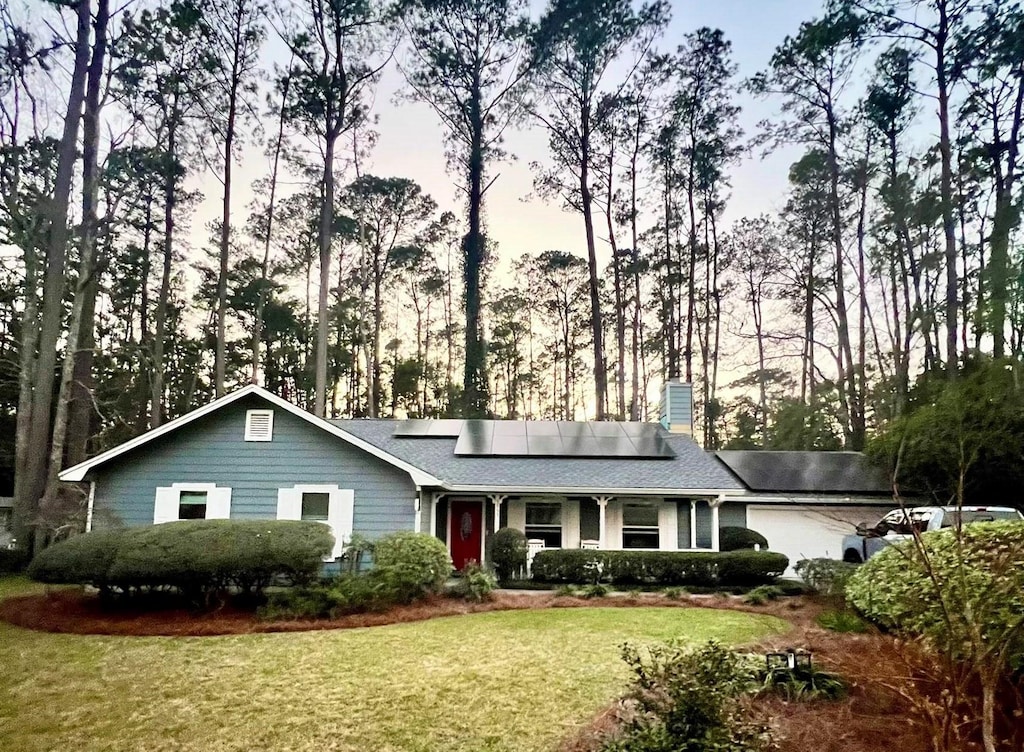 single story home with a garage, a chimney, a front lawn, and solar panels