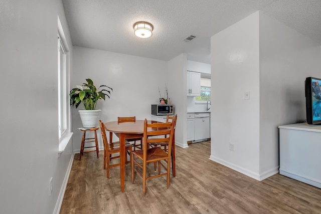 dining space featuring sink, a textured ceiling, and light wood-type flooring