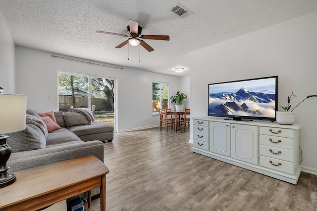 living room with ceiling fan, a textured ceiling, and light wood-type flooring