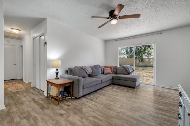 living room with ceiling fan, a textured ceiling, and light wood-type flooring