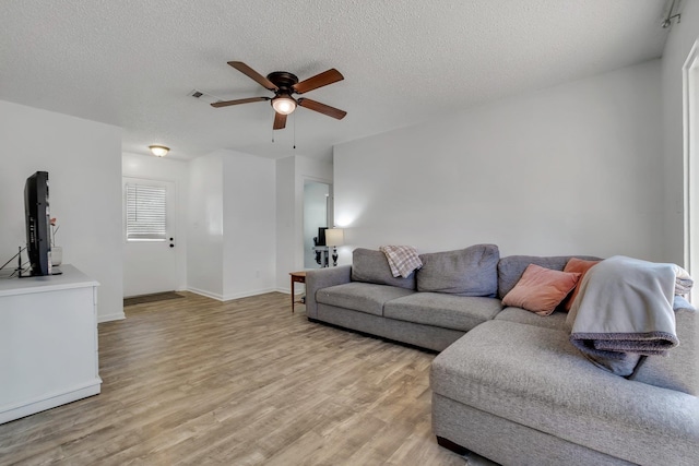 living room with ceiling fan, a textured ceiling, and light wood-type flooring