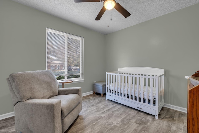 bedroom featuring a nursery area, ceiling fan, light hardwood / wood-style floors, and a textured ceiling