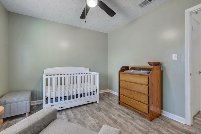 bedroom featuring light hardwood / wood-style flooring, a textured ceiling, a crib, and ceiling fan