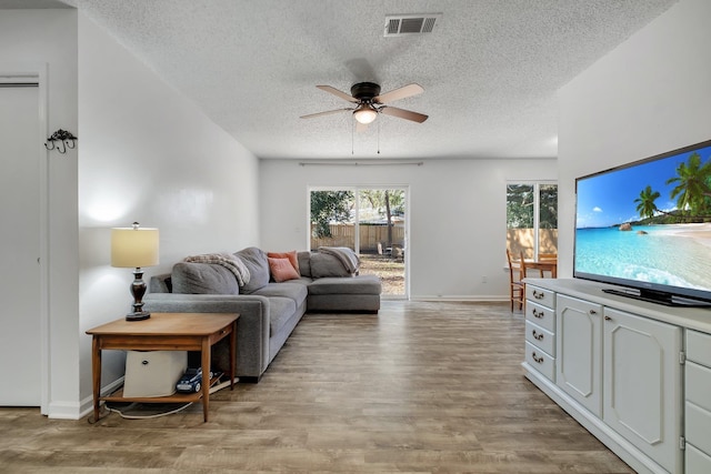 living room featuring ceiling fan, light hardwood / wood-style flooring, and a textured ceiling