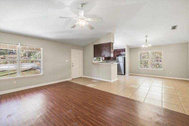 unfurnished living room featuring ceiling fan with notable chandelier, light tile patterned floors, a healthy amount of sunlight, and lofted ceiling