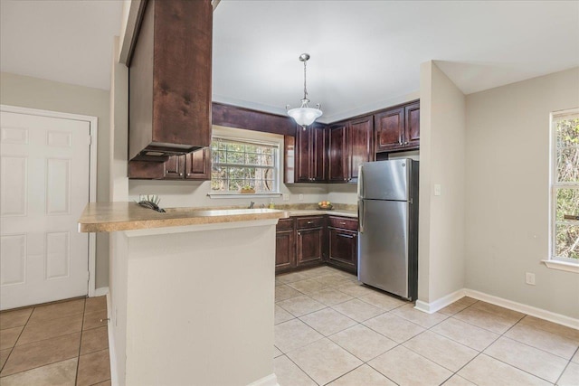 kitchen featuring kitchen peninsula, decorative light fixtures, stainless steel refrigerator, and a healthy amount of sunlight