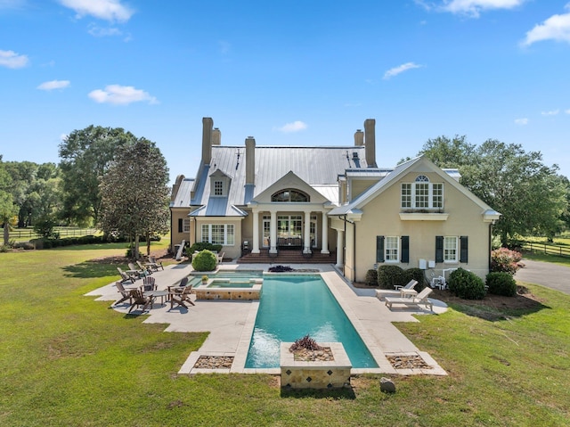 back of house with a patio, metal roof, a lawn, a chimney, and stucco siding