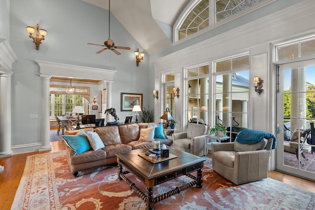 living area with wood finished floors, baseboards, ornate columns, a ceiling fan, and a high ceiling