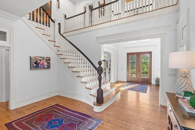 foyer entrance with stairway, french doors, baseboards, a towering ceiling, and wood finished floors