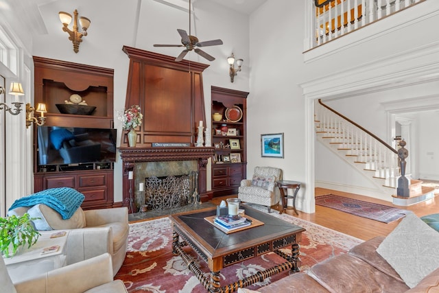 living area with wood finished floors, stairs, a fireplace, a ceiling fan, and a high ceiling