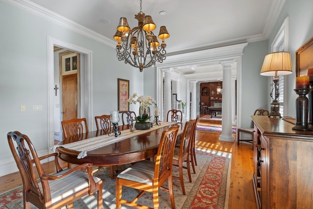 dining room featuring an inviting chandelier, light wood-style floors, crown molding, and decorative columns