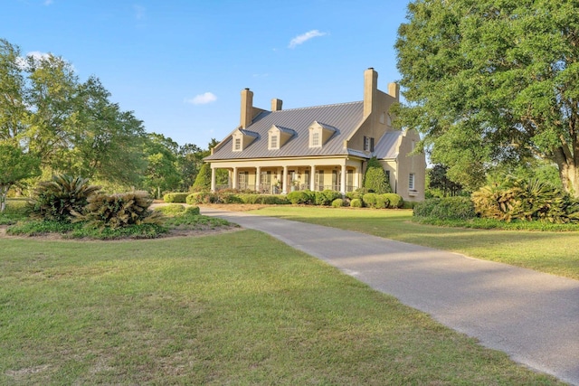 cape cod house with a chimney, covered porch, a front yard, and metal roof