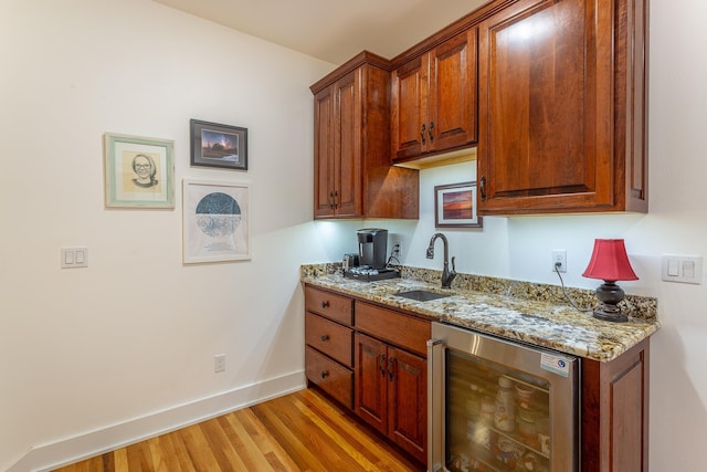 kitchen featuring light stone countertops, sink, beverage cooler, and light hardwood / wood-style flooring