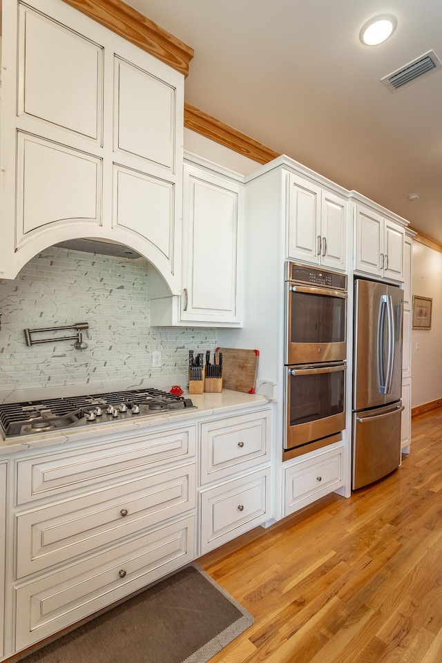 kitchen with white cabinets, light hardwood / wood-style flooring, ornamental molding, tasteful backsplash, and stainless steel appliances