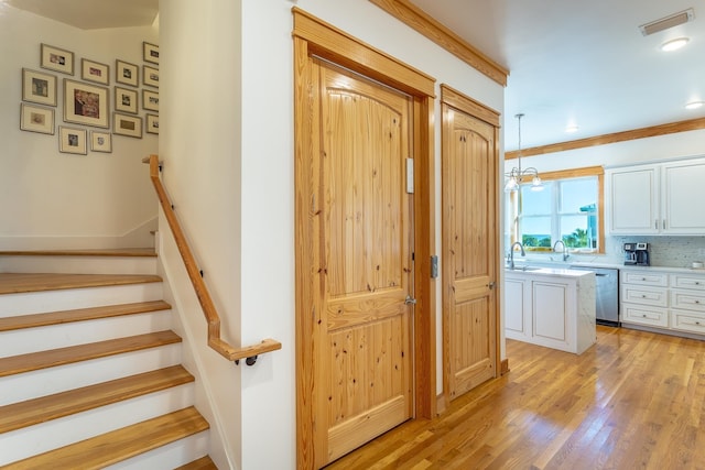 staircase featuring hardwood / wood-style flooring, an inviting chandelier, crown molding, and sink